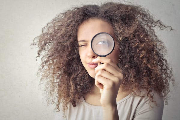 Girl looking into a magnifying glass; concept of employee background checks in Singapore