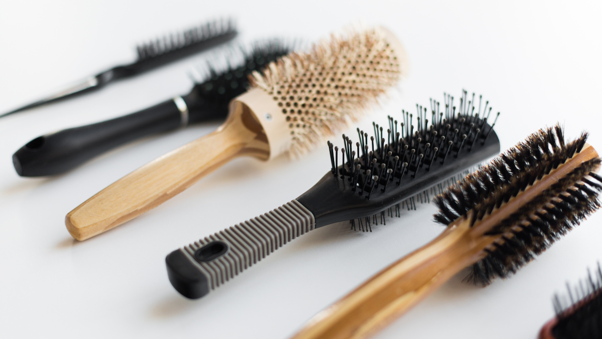 A variety of hairbrushes, including wooden and bristle designs, arranged on a white surface, showcasing diverse hairstyling tools.