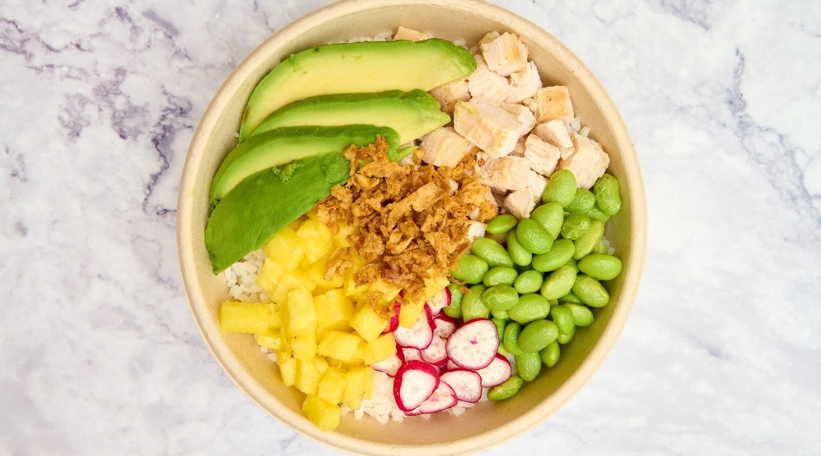 Colorful poke bowl featuring fresh avocado slices, diced chicken, edamame, pineapple, radishes, and crispy onions over a bed of rice. This vibrant and nutritious meal is an ideal choice for healthy eating in Mississauga, highly recommended by our registered dietitian.