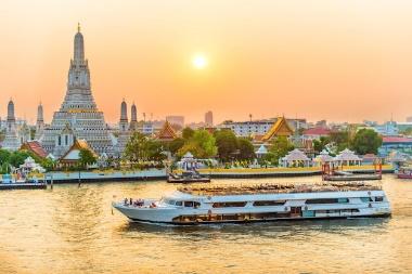 Beautiful temple of dawn or wat arun and boats on chao phraya river at sunset with shining sun bangkok thailand