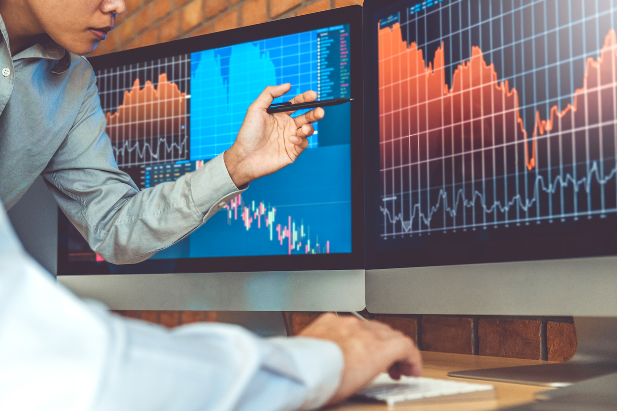 Profissionais analisando gráficos financeiros em telas de computador com indicadores de variação e oscilação — imagem ilustrativa para conteúdo sobre o indicador estocástico no day trade, no blog da CM Capital.