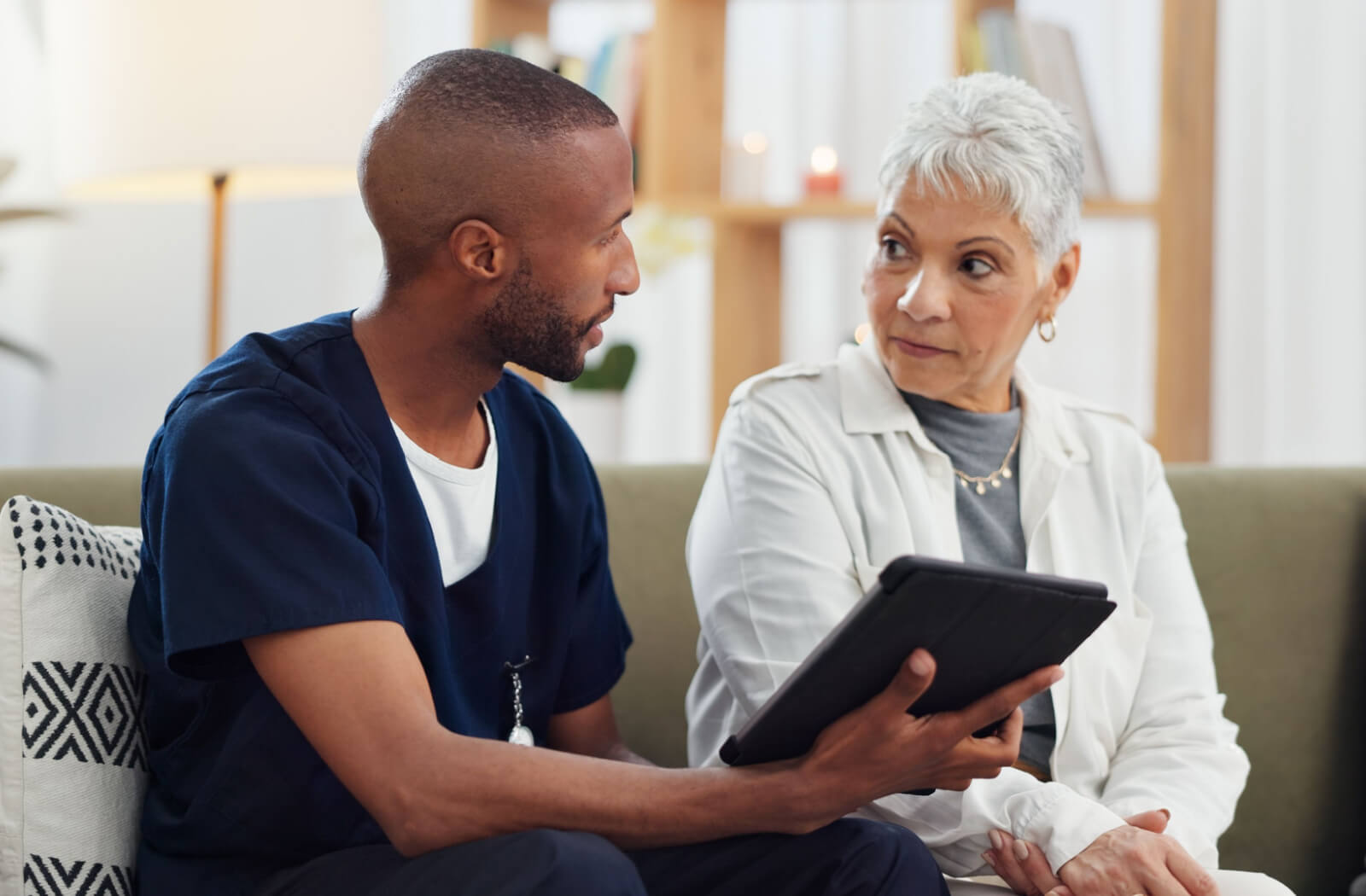 A caregiver holding a tablet and showing a resident in senior living how AI-enabled fall detection keeps them safe.