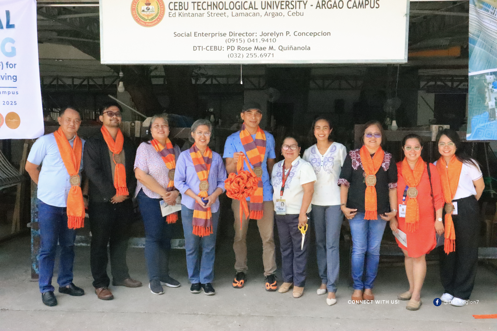 A group of people standing in front of the Cebu Technological University - Argao Campus building, with a sign displaying contact details for the Social Enterprise Director and DTI-Cebu representative.