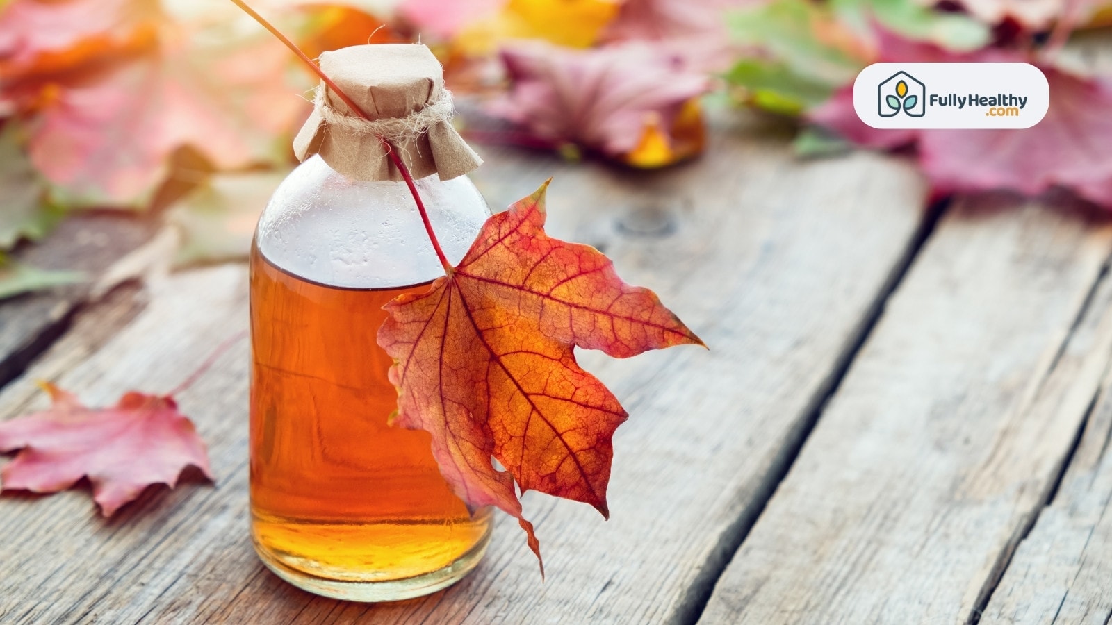 Glass bottle of maple syrup with autumn leaves on table