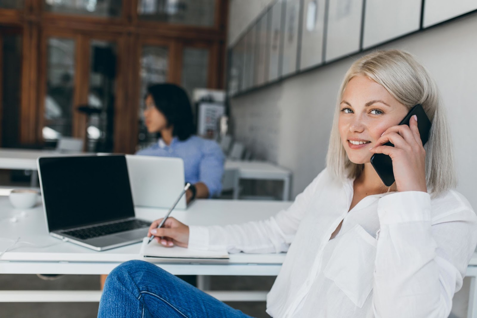 Woman speaking on the phone while managing a pay-per-call campaign at her desk, using a laptop and taking notes