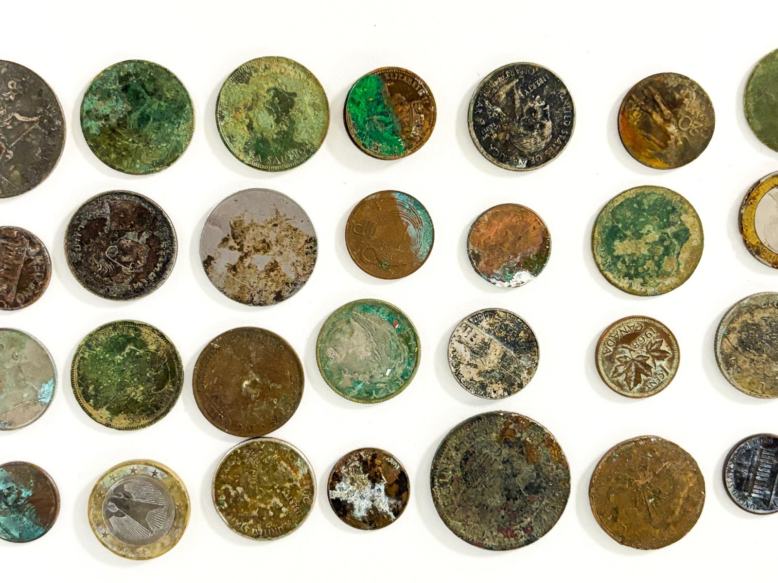 rows of coins from across the world that have water damage and corrosion.