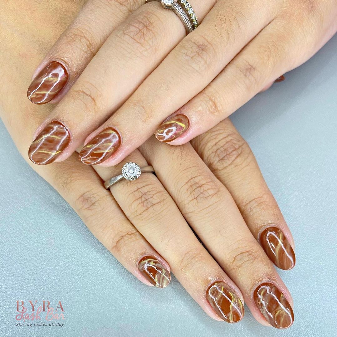 Close-up of hands with marble-designed manicure, showcasing detailed nail art with white and gold accents.