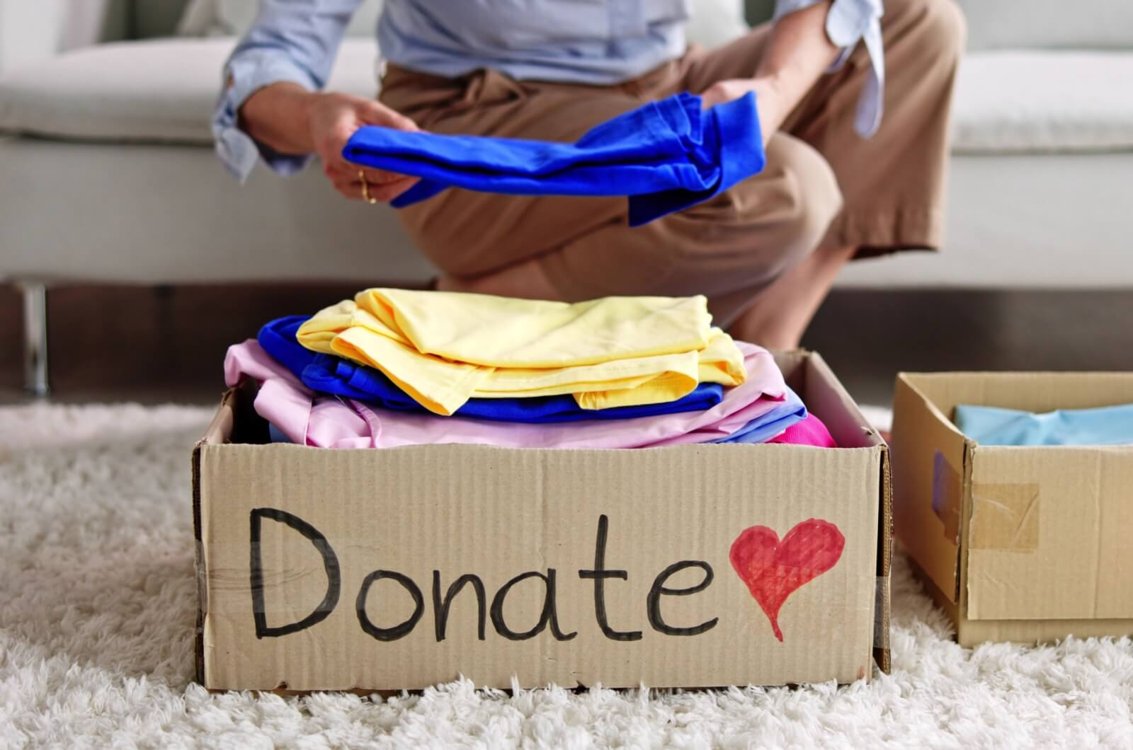 A close-up image of a person putting clothing into a box labelled for donation.