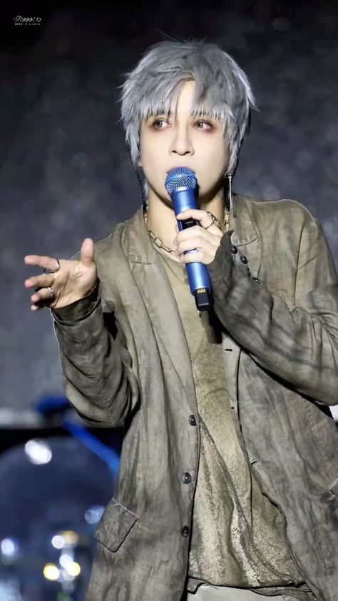 This contains an image of Joker Xue with grey hair holding a microphone