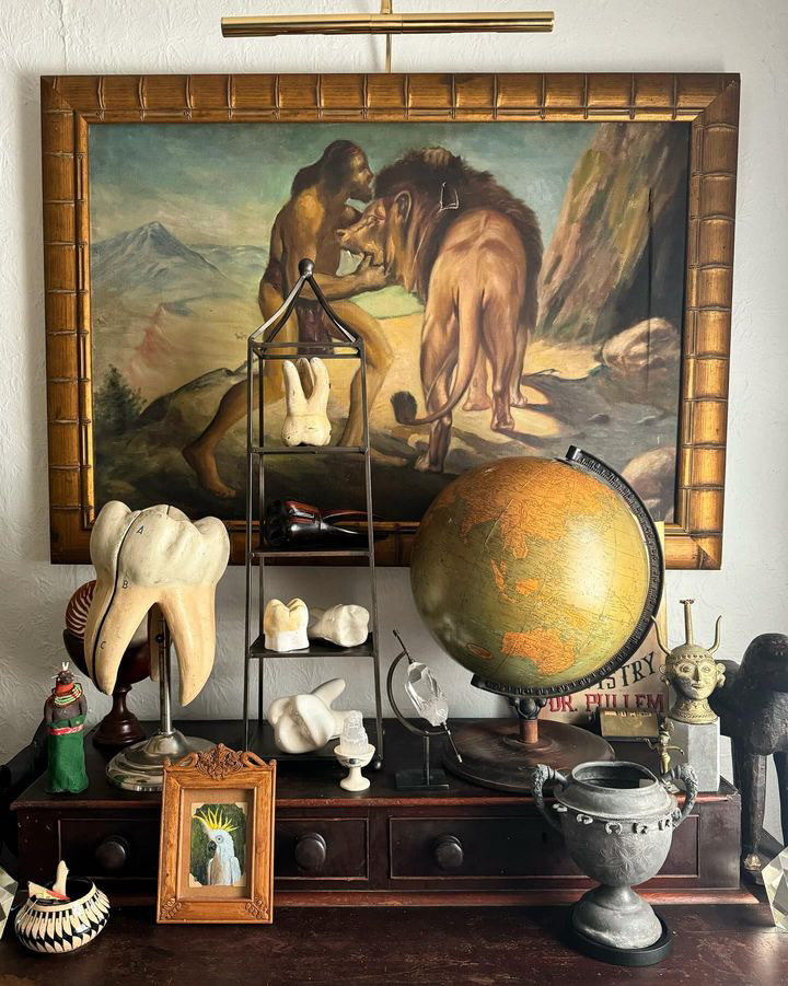 A large painting depicting a cave man and a lion hung above an assortment of decorative items.