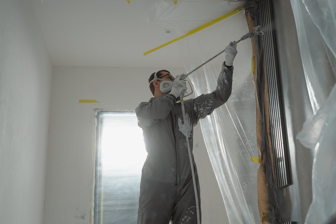 Worker in protective gear using spray tool, highlighting safety protocols in risk management systems.