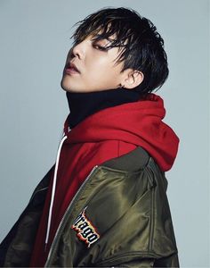 This contain an image of G-Dragon with black hair wearing a red scarf and jacket, looking off to the side