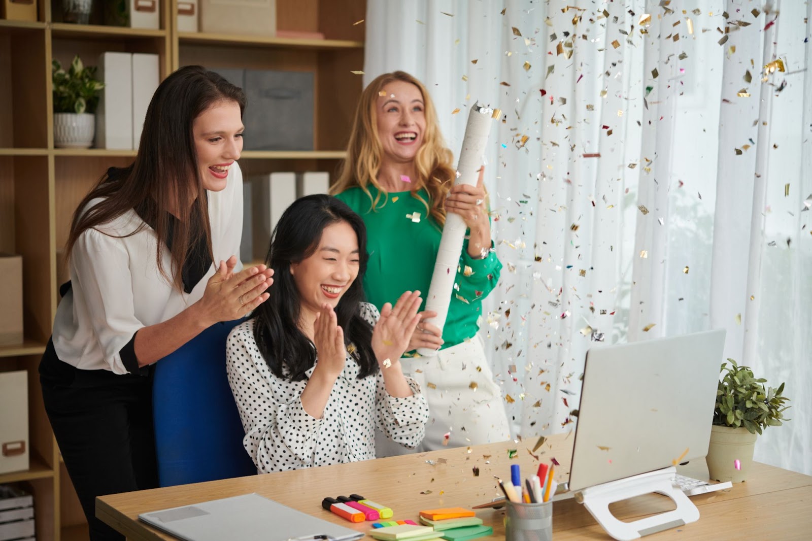 Women smiling and clapping with confetti coming down. 