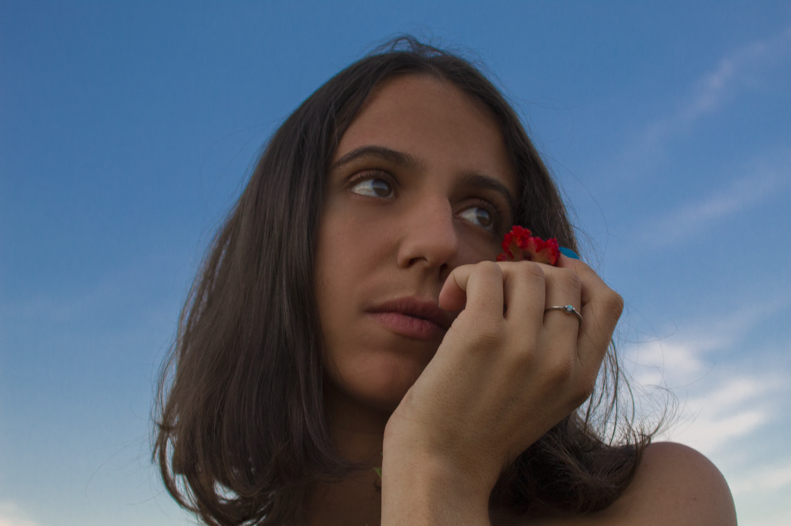 Uma mulher segurando uma flor perto do rosto mostrando um anel na mão 