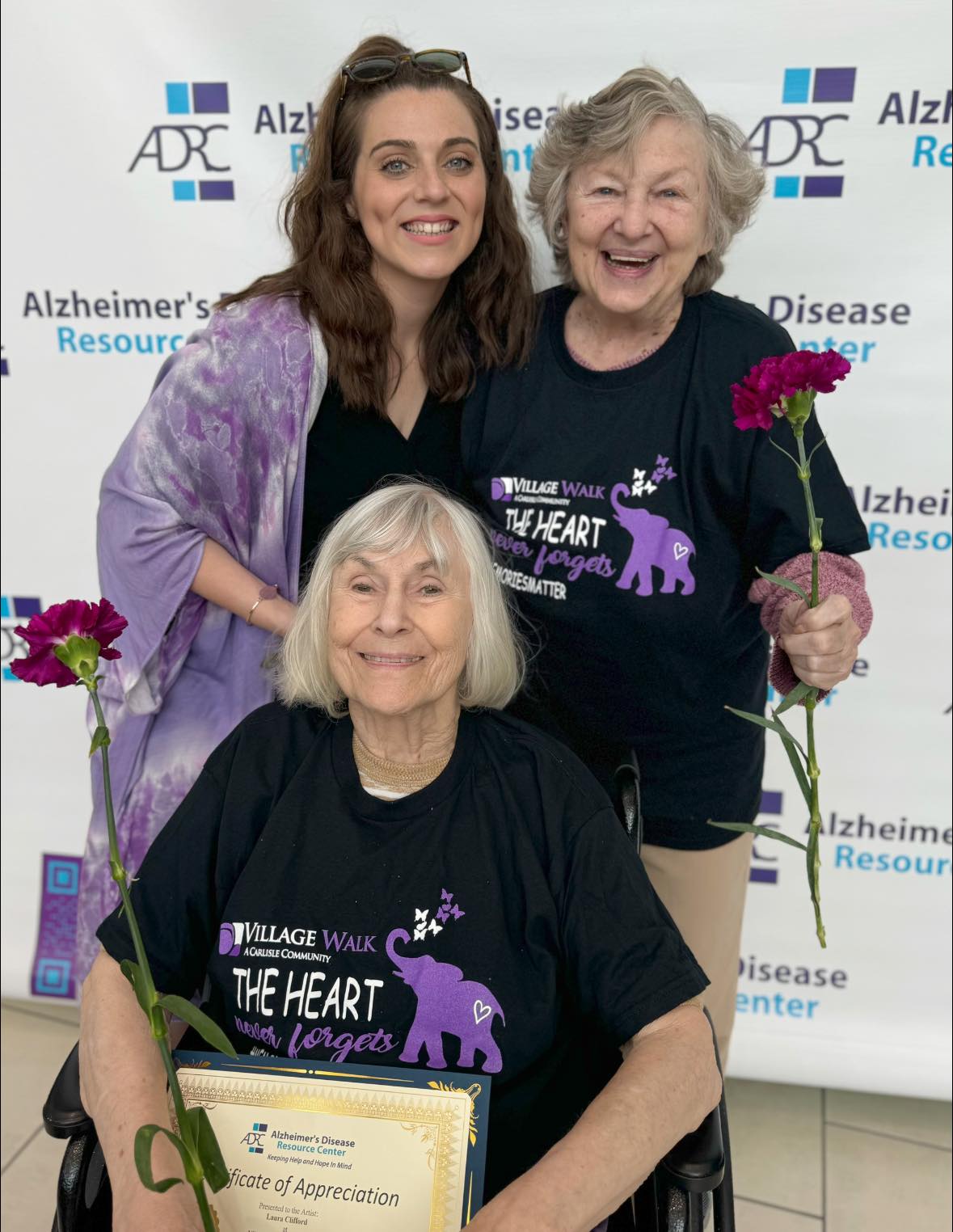 An assisted living worker smiling with two assisted living residents at an Alzheimer's awareness event