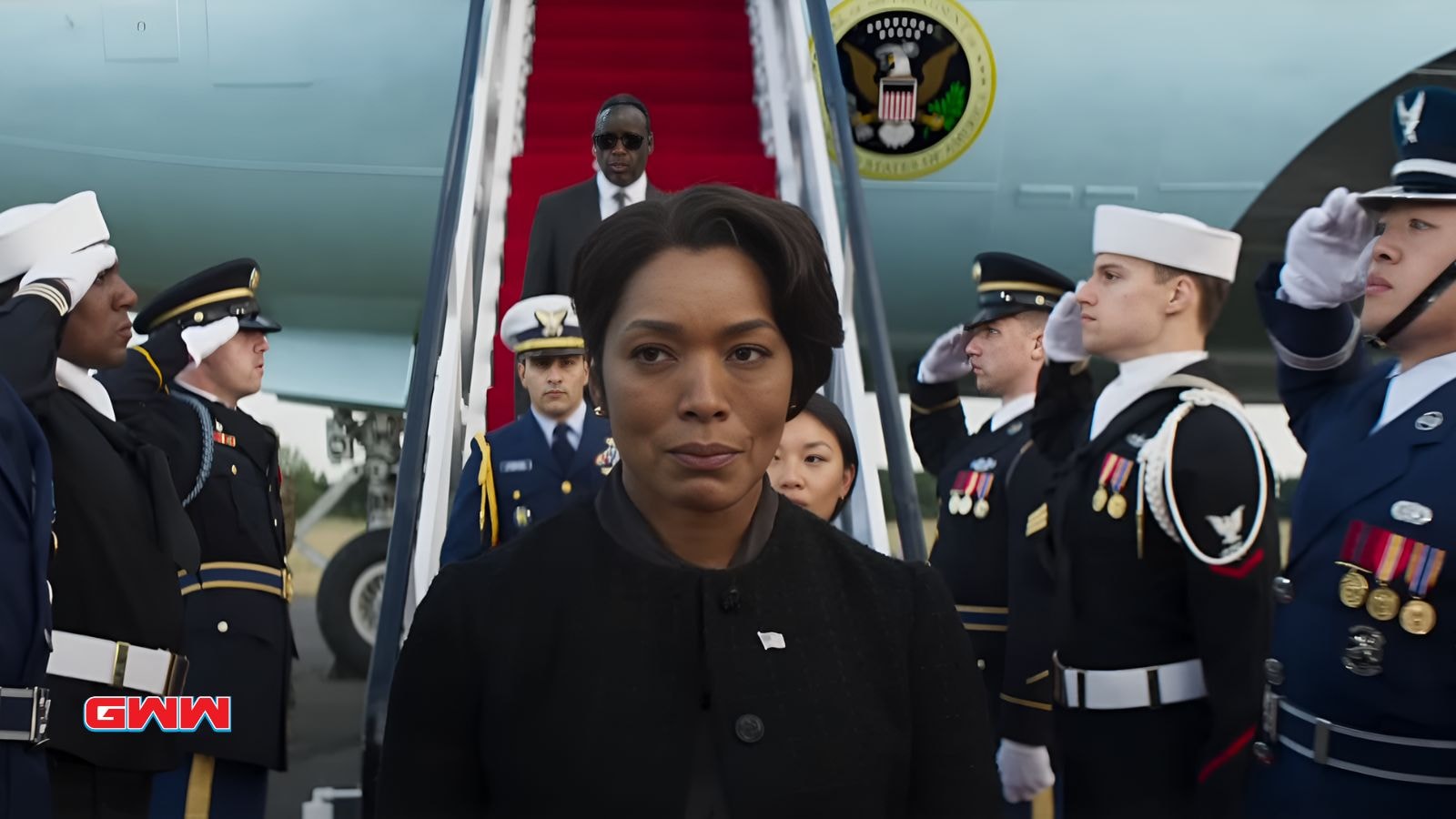 Angela Bassett steps off a plane, surrounded by military personnel.