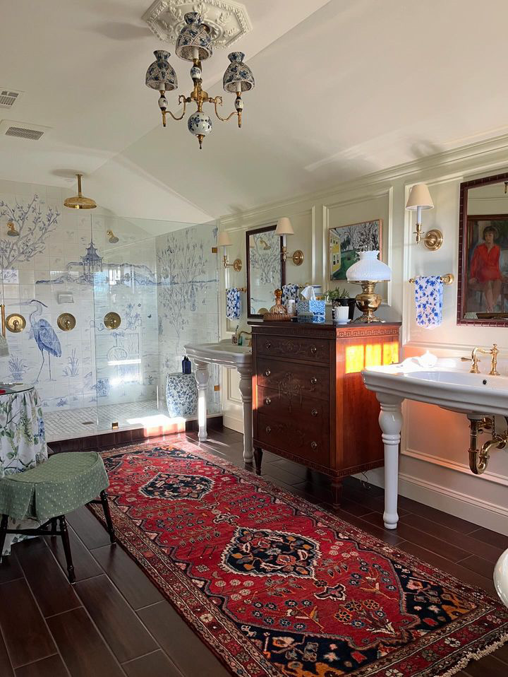 A brightly decorated traditional bathroom features porcelain pedestal sinks, chest of drawers, Persian rug and blue and white accessories