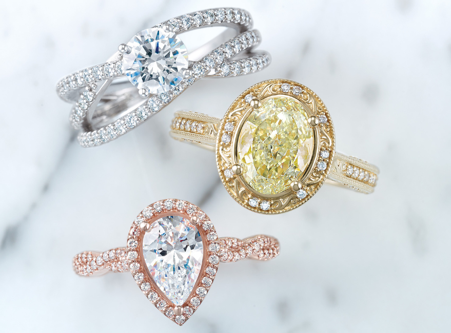 Three engagement rings in white gold, yellow gold and rose gold on a white a grey marble background