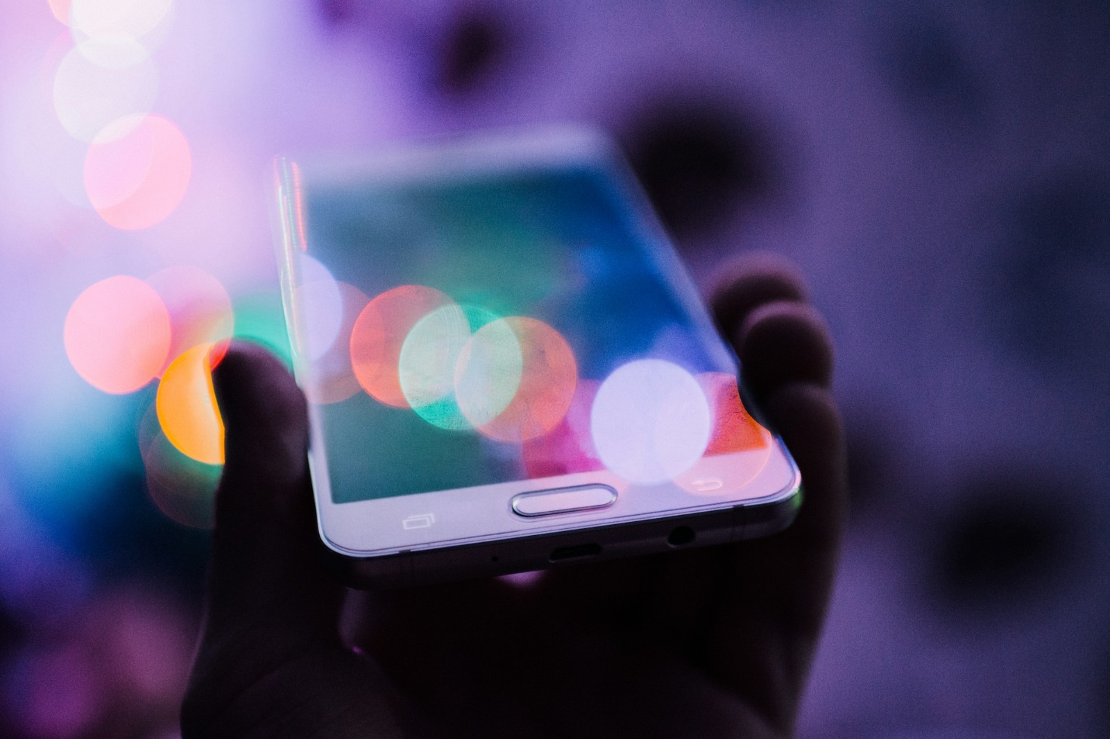 A close-up of a smartphone screen with colorful bokeh lights in the background. It symbolizes digital distractions contributing to parental stress.