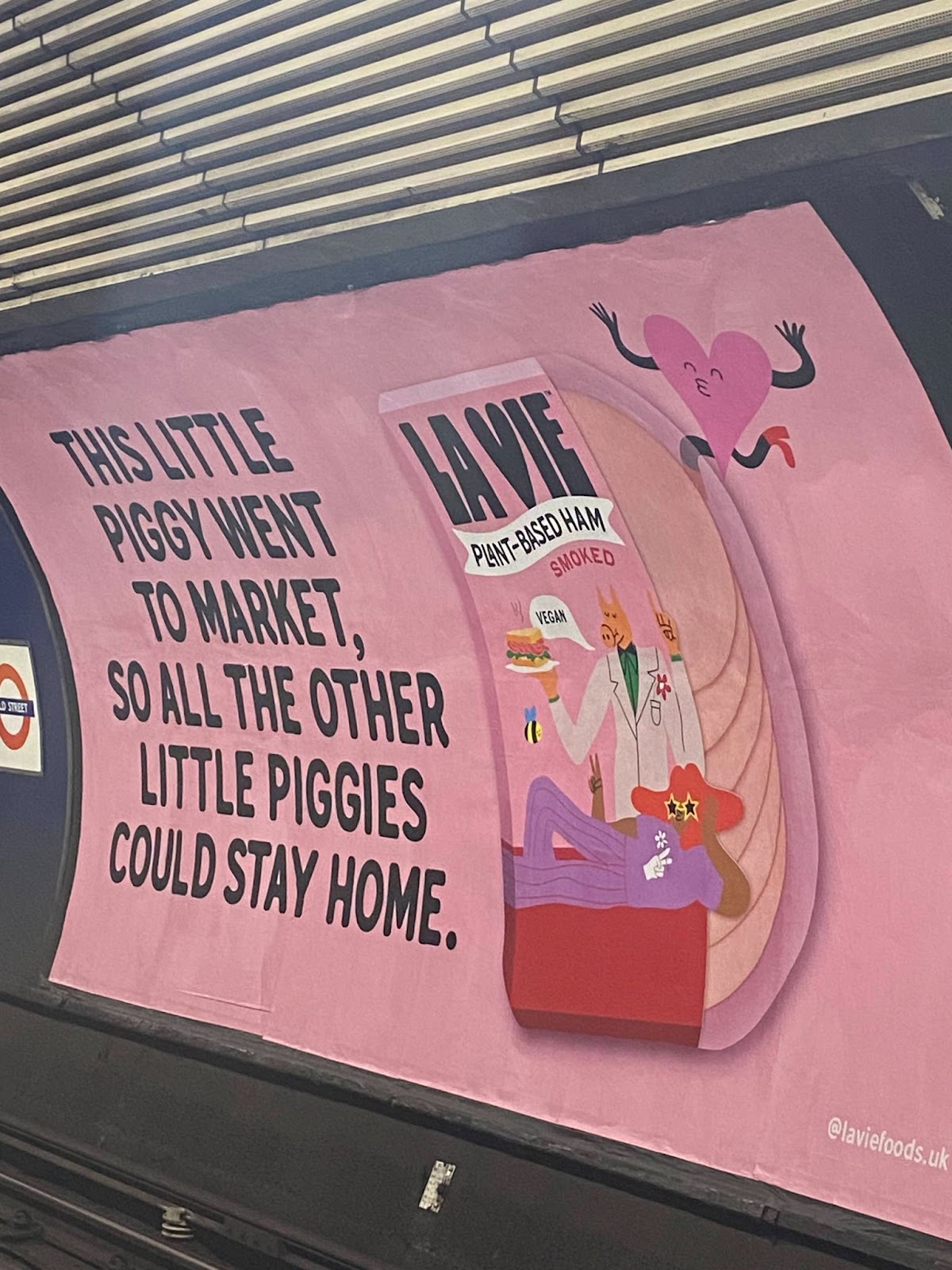 A billboard in the London Underground which is a pink background, an image of their plant based meat in its packaging with the play on the nursery rhyme next to it "This little piggy went to market, so all the other little piggies could stay at home". 