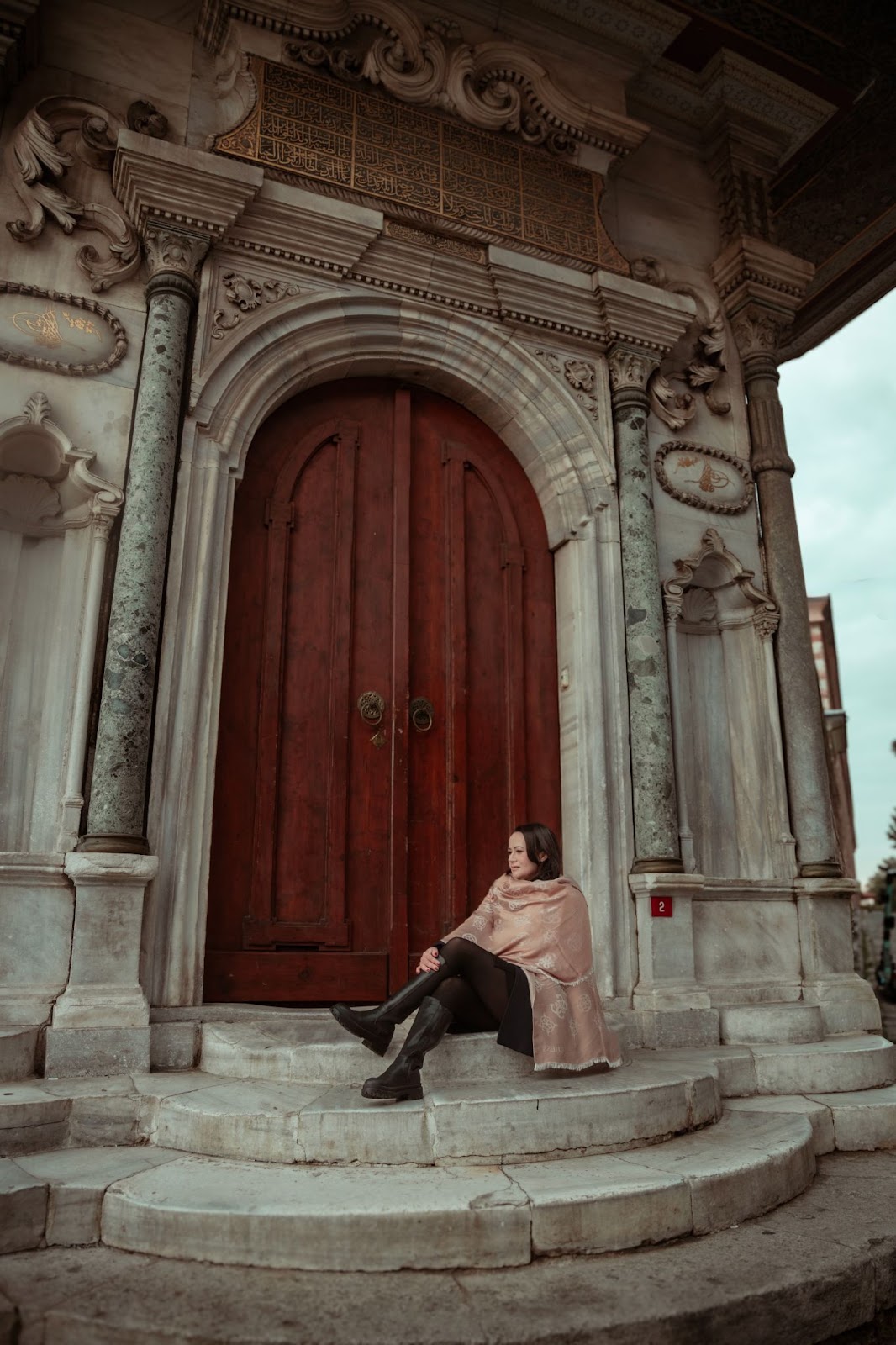 Elegant lady sitting on steps, framed by carved doorway.
