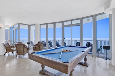 A bright room overlooking the ocean on a penthouse floor with a pool table in the forefront.