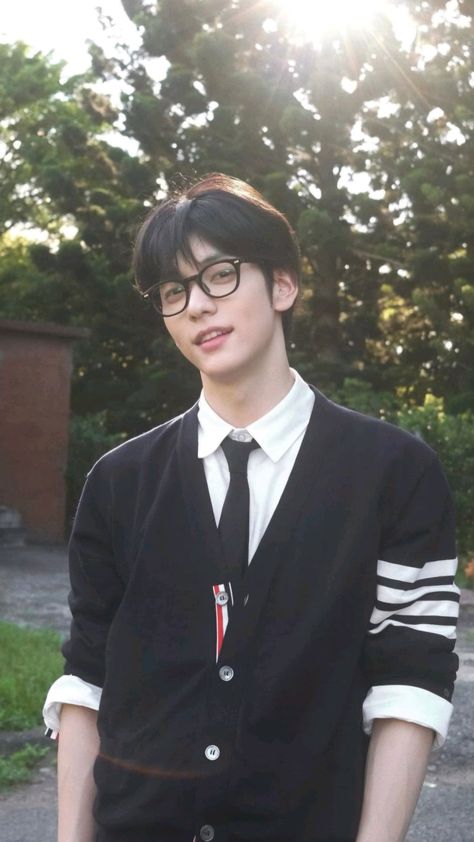 This contains an image of Soobin  wearing glasses and a black sweater is standing in front of some trees