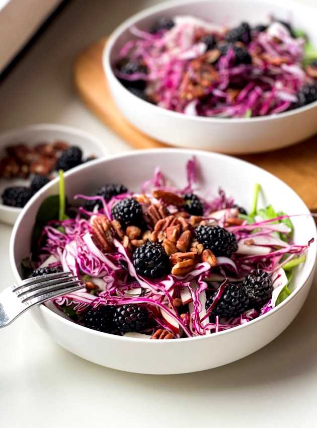 Salade avec chou rouge râpé, mûres, pacanes et verdure dans un bol blanc.
