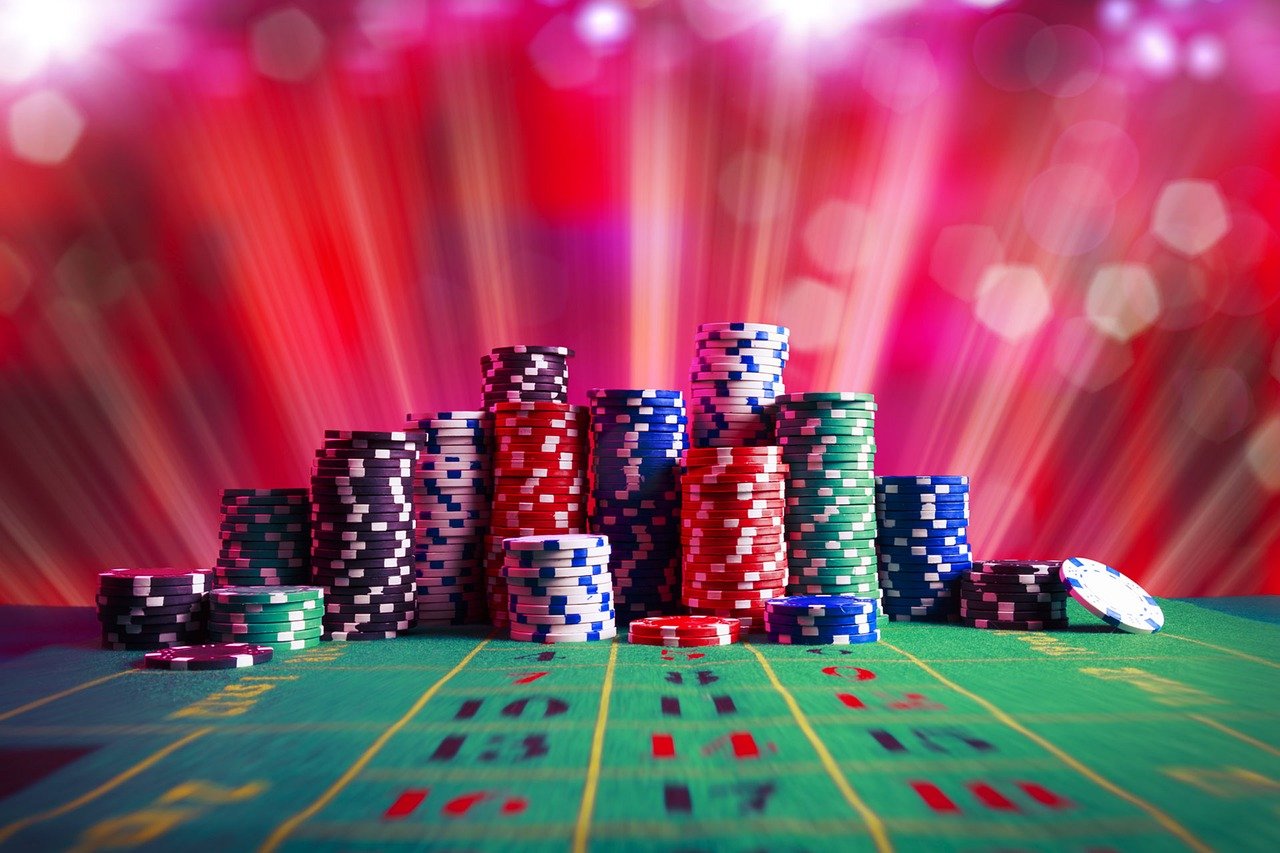 A vibrant display of colorful casino chips stacked on a roulette table with a red and purple light background, creating an exciting casino atmosphere.