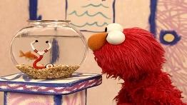 A red puppet looking at a fish bowl

Description automatically generated