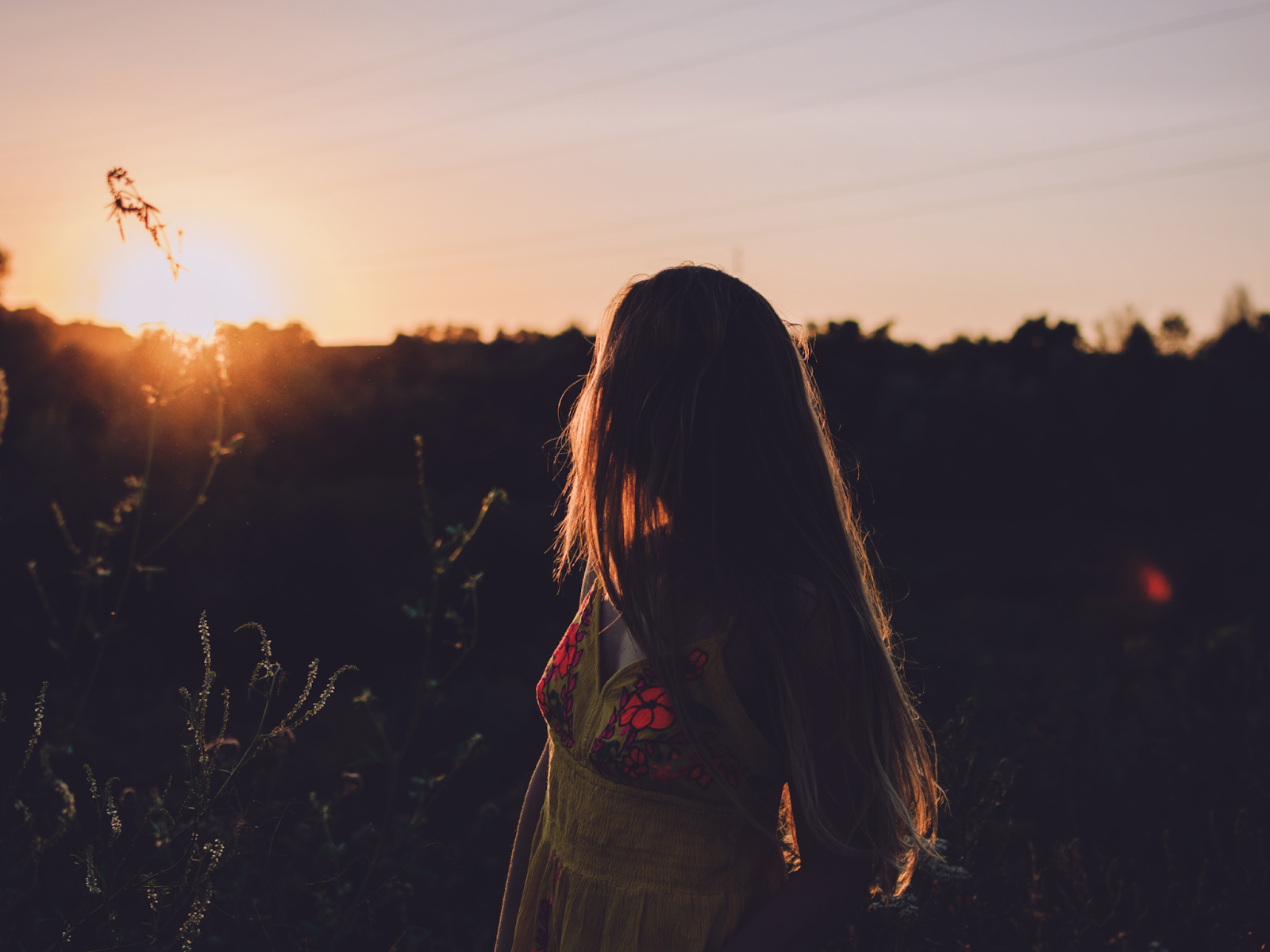 A woman stands in a meadow and looks over her shoulder at the setting sun
