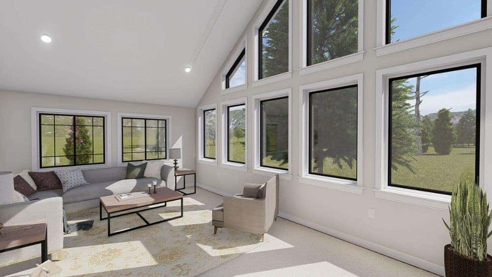 The sunroom offers gray seats, wood-top tables, and a printed area rug over carpet flooring.