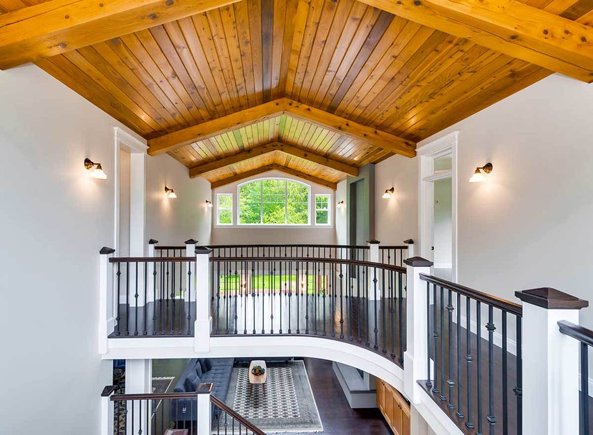 Balcony bridge with wrought iron railings and a cathedral ceiling clad in wood planks.