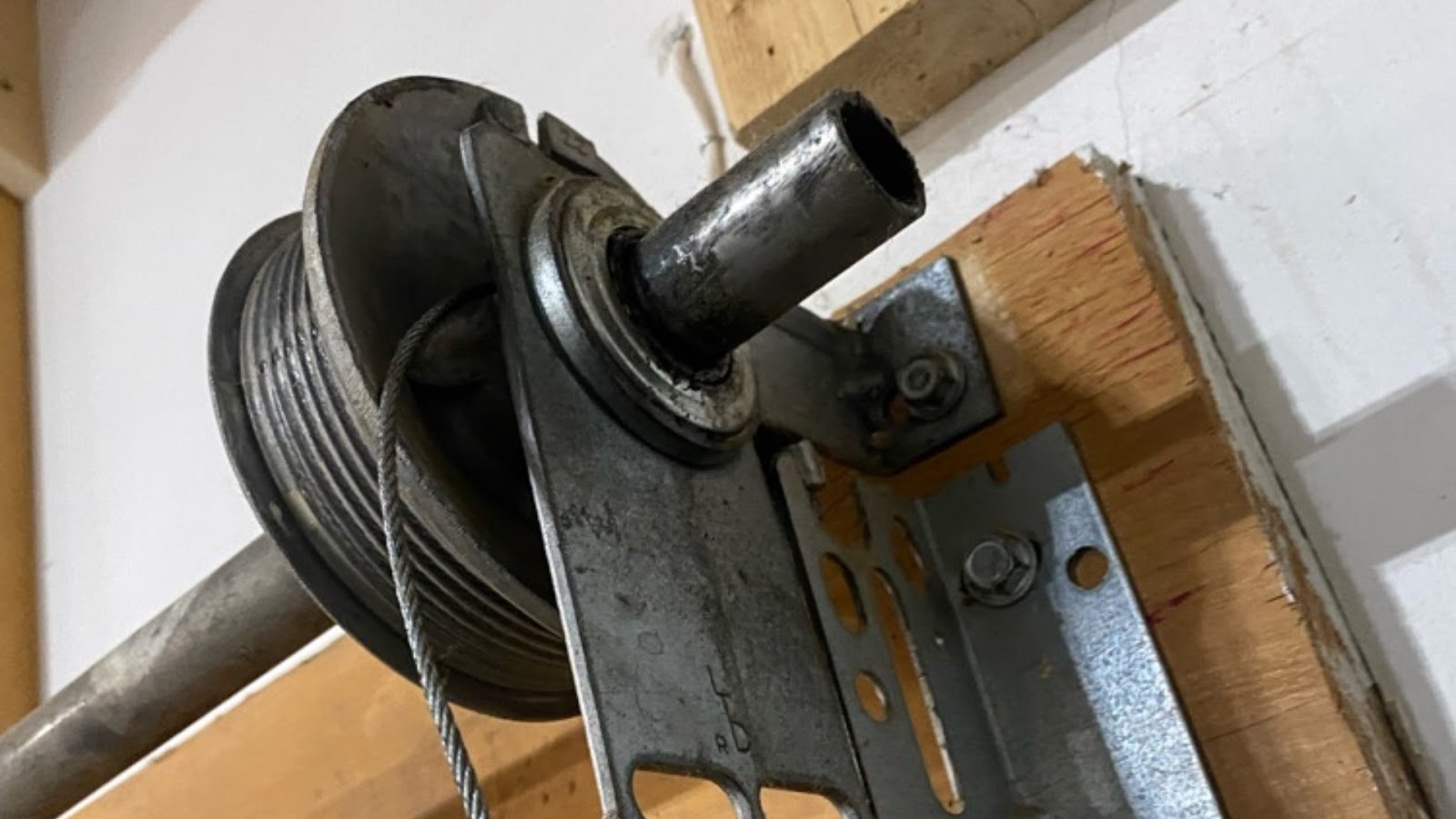 Frayed and worn garage door cable on the drum, needing replacement.
