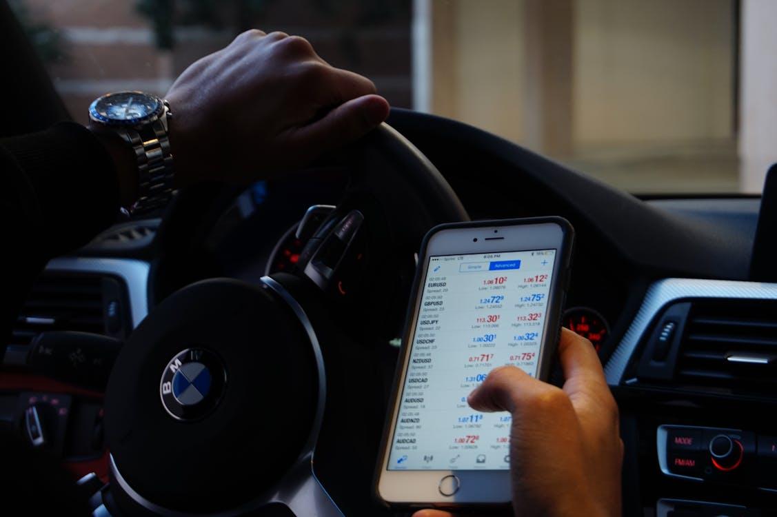 Free Person using mobile phone for currency trading while driving BMW car. Stock Photo