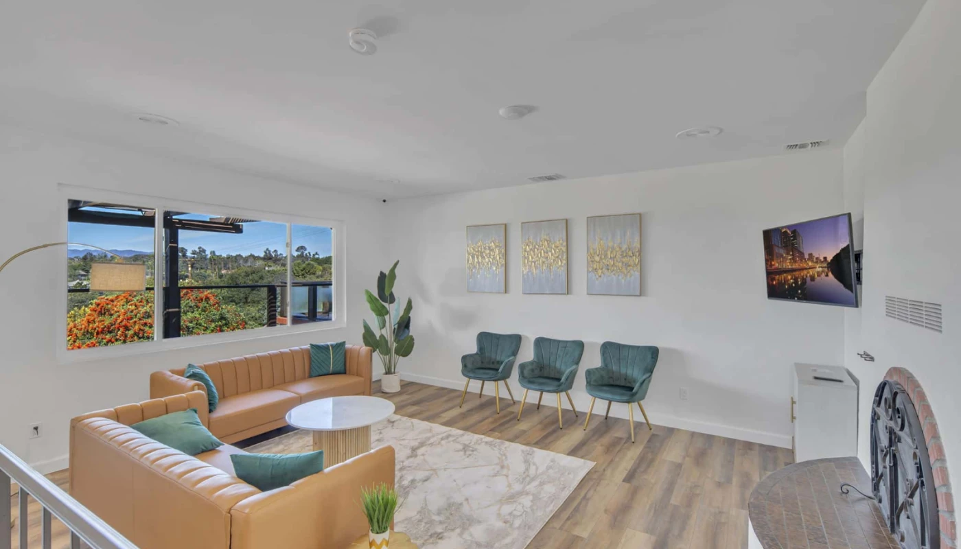 Interior view of a California mental health treatment center, showing a modern room with a tan sofa, teal chairs, and mountain views through large windows.