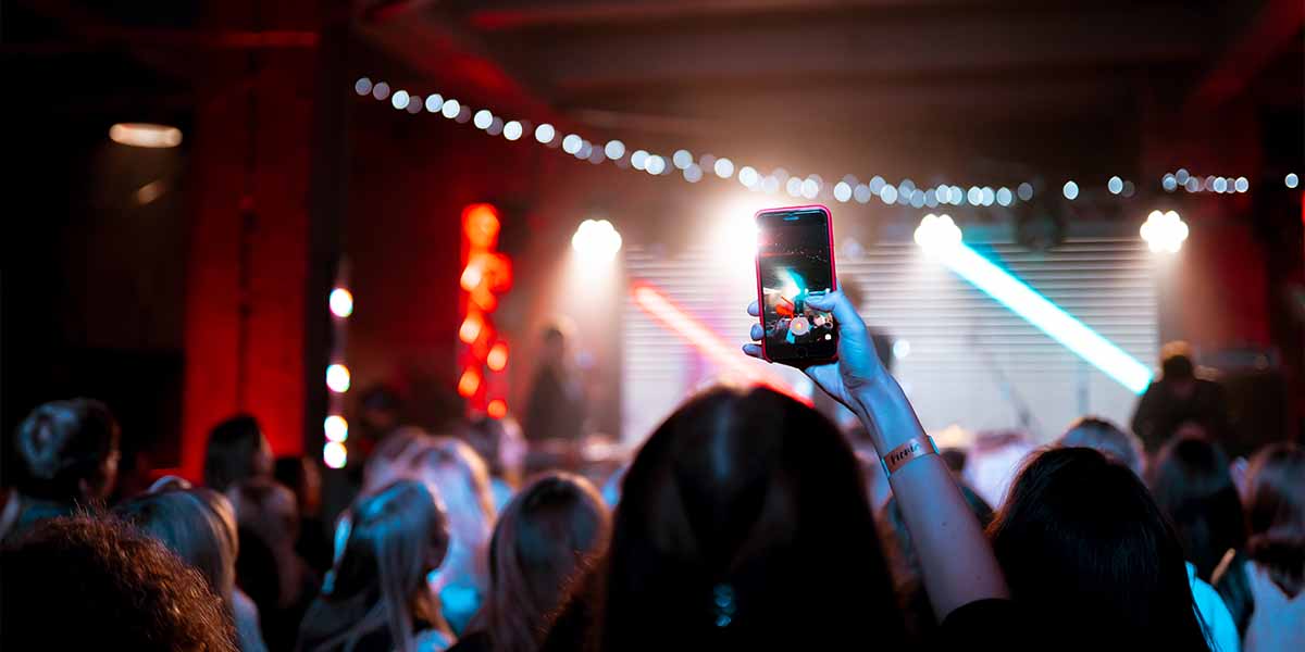 A person snaps a picture at a concert, highlighting the lively performance and enthusiastic audience.