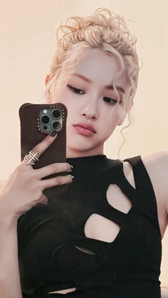 This contains an image of BLACKPINK Rosé's  holding a cell phone in her hand and wearing a black dress with cutouts on it