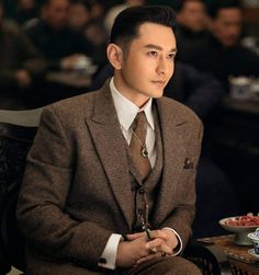 This contains an image of Huang Xiaoming in a suit and tie sitting at a table