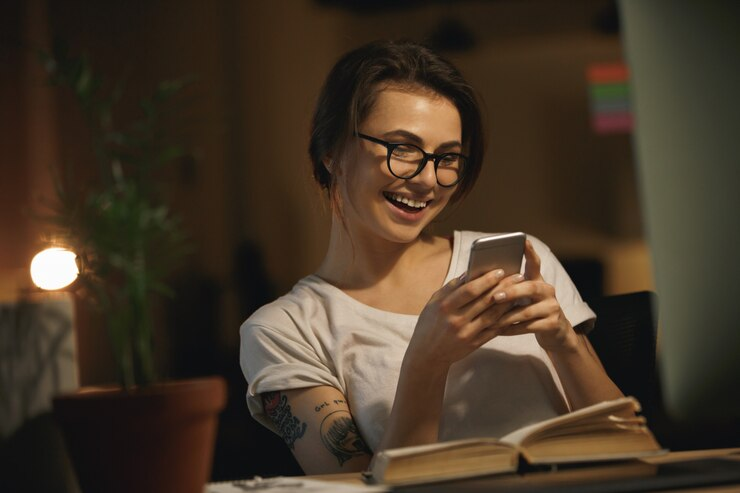 Happy woman sitting indoors at night using phone