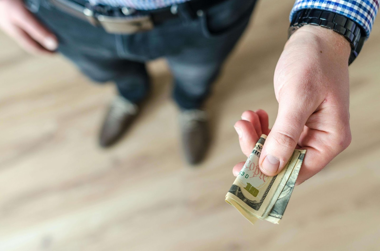 A man holding out a folded dollar note.