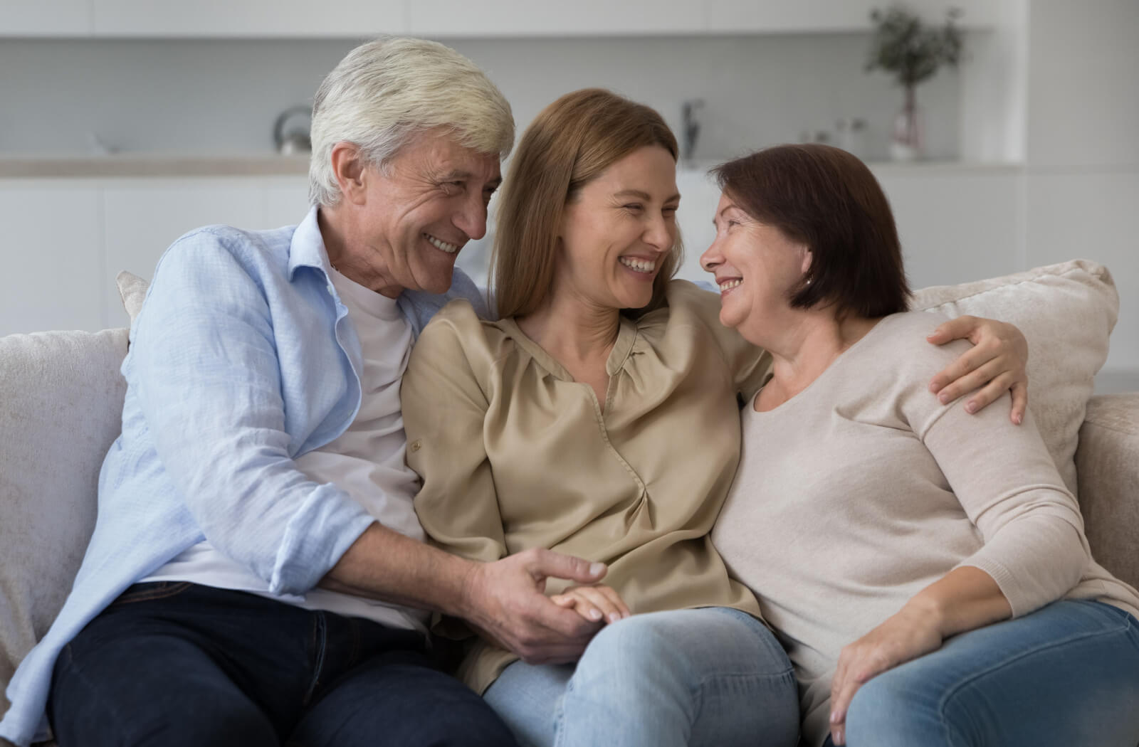 An adult visiting their older parents in senior living, smiling and hugging each other on the couch.