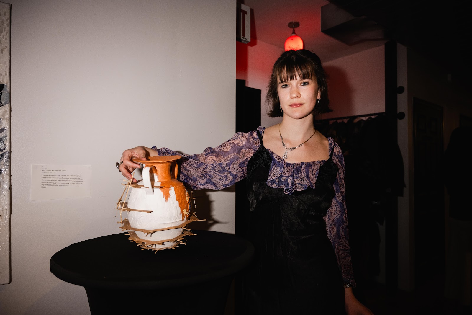 Poppy Thomas stands next to a vase in a dim background.