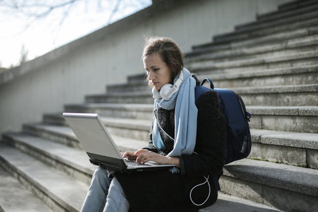 A woman sitting on concrete stairs using a laptop