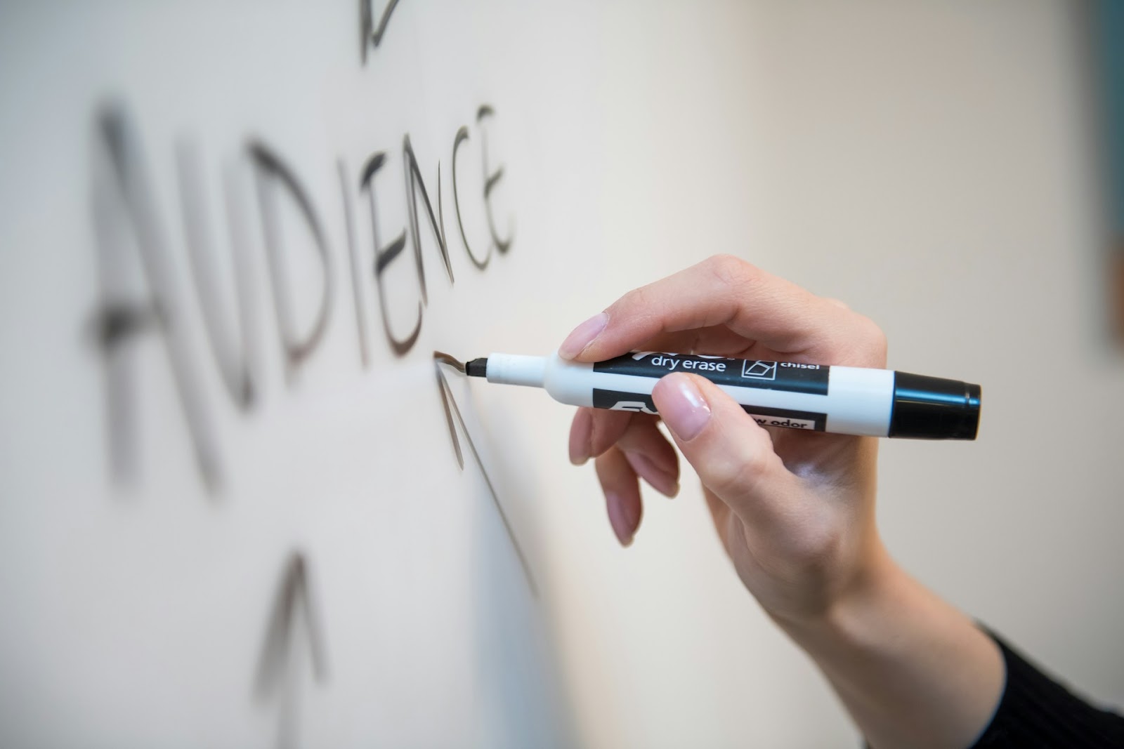 A hand writing the word 'Audience' with a dry erase marker on a whiteboard, representing a focus on marketing strategies