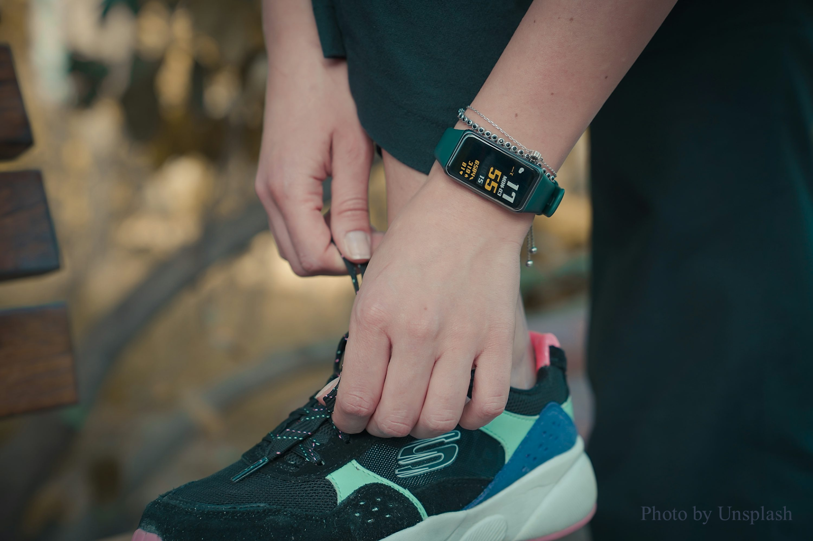 Close-up of a person tying their running shoes while wearing a fitness tracker smartwatch, displaying health and activity metrics.