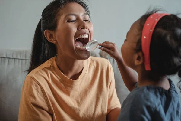 A child examining the teeth of an adult closely with a magnifying glass in a bright setting.