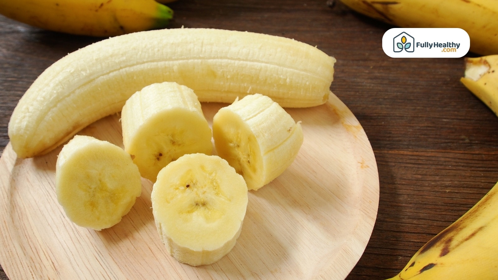 Sliced banana on wooden board with unpeeled banana in background