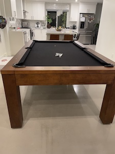 Pool table in a basement with a kitchen in the background.