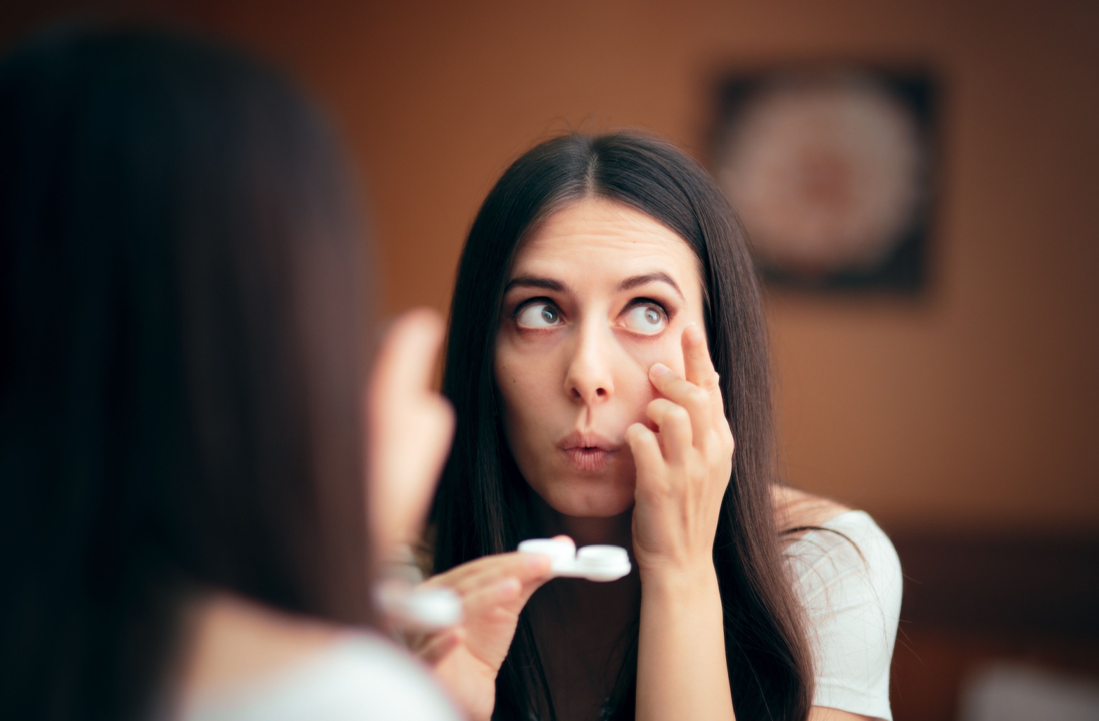 A person looking into a mirror while inserting or adjusting their lens.